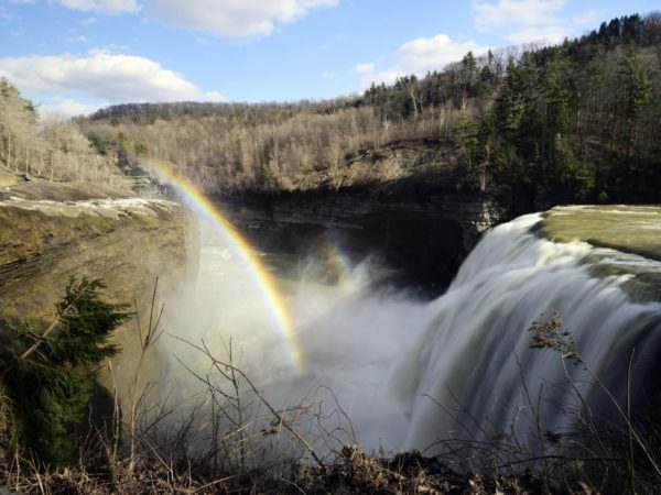 A large waterfall and rainbow surrounded by brown hillsides