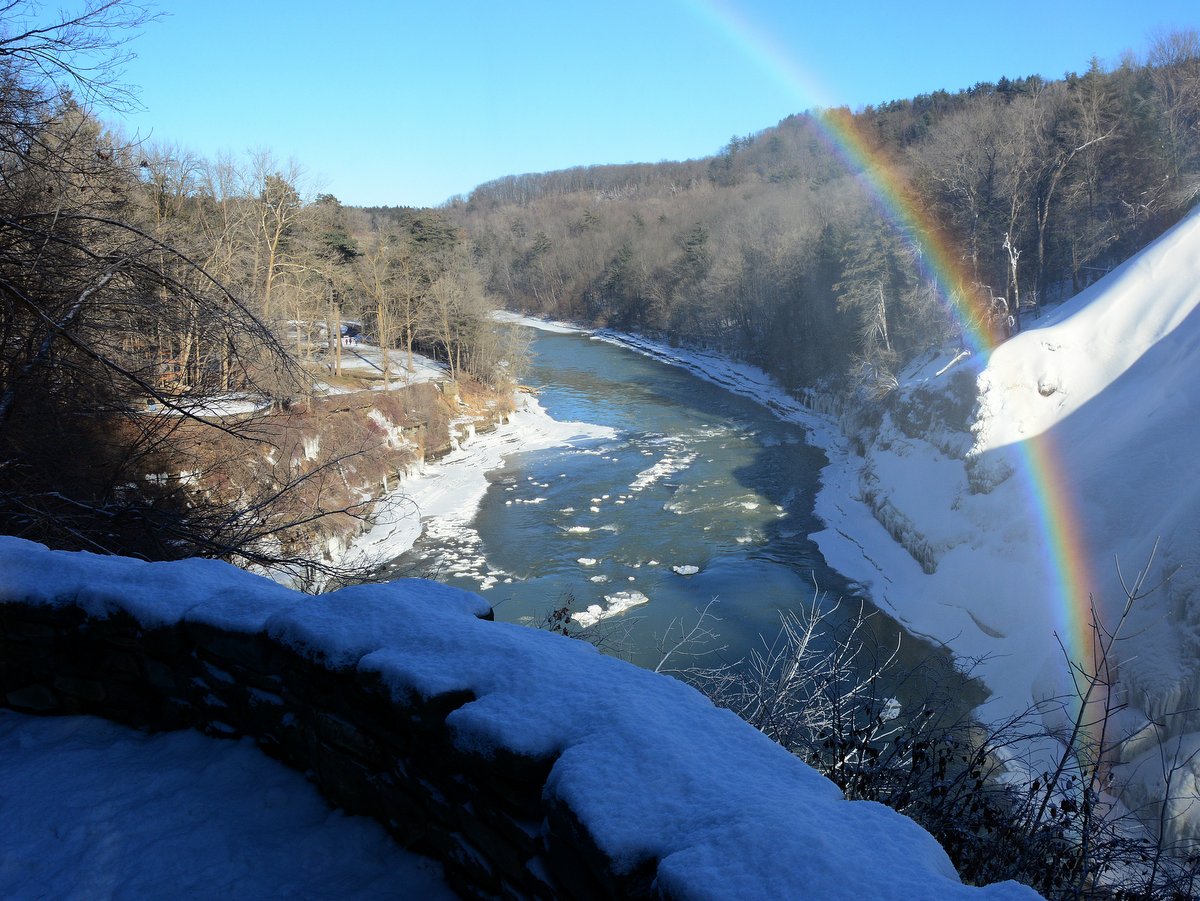 A river with snow covered hills and a rainbow