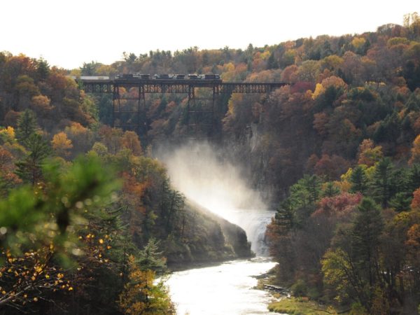 A misty waterfall with an overarching railroad bridge and train cars