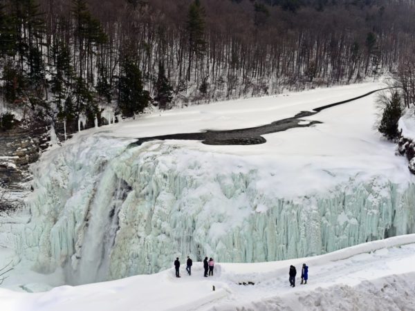 People standing on the edge of a gorge with a frozen waterfall in winter