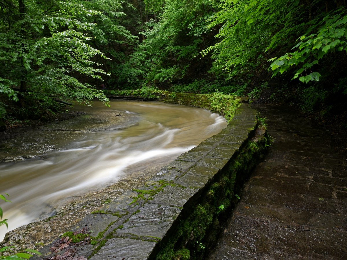 A rushing creek and trail separated by a stone wall