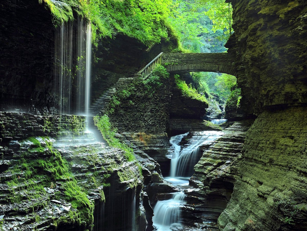 A large gorge with waterfalls and a stone bridge