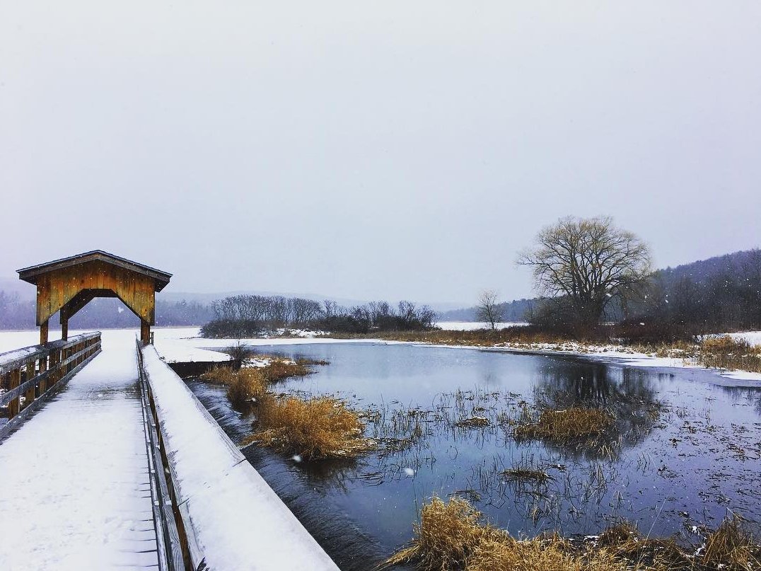 A snow covered footbridge and covered wooden shelter extending into a lake